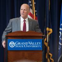 Dean Potteiger talking at a GVSU podium in focus, people's heads out of focus in the foreground